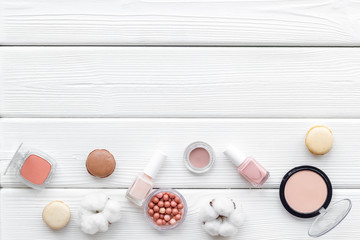 Make-up artist desk with powder, decorative cosmetics and macaroon cookies on white wooden background top view mokeup