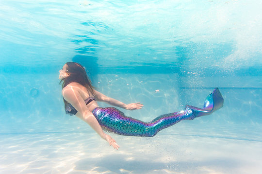 Woman on family vacation swims gracefully in pool wearing colorful fish scale mermaid tail monofin