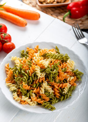 Multicolored pasta with vegetable on wooden background ve vegetables