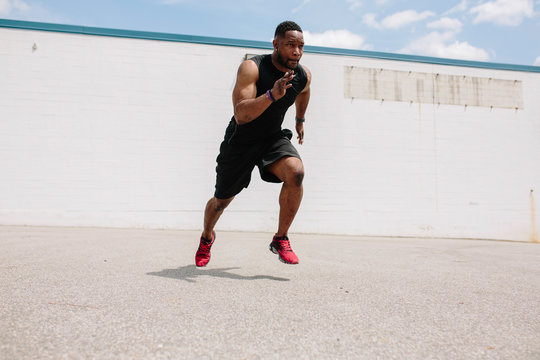 Fit athlete practicing sprints and jumps in a parking lot
