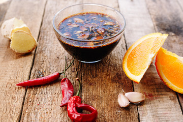 Soy sauce with chilly pepper, garlic, ginger and orange. Wooden table. Homemade. Diet.