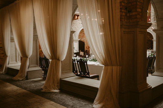 Moody chateau interior with hanging drape curtains and wooden chairs for dinner table set up