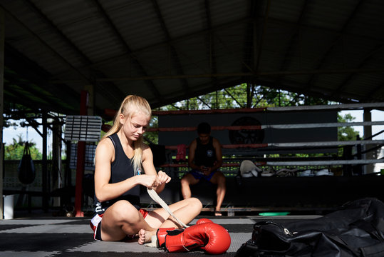 Muay thai female boxer wrapping strap around hand. - Powered by Adobe