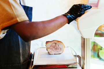Employee weighing porchetta in a grocery store.