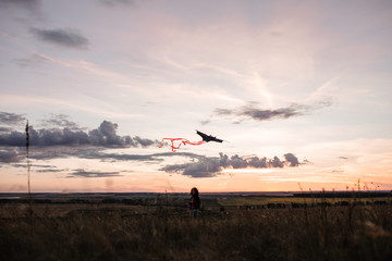 A young girl launches a kite into the sky in a field at sunset