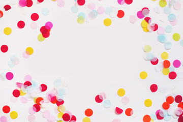 Colorful paper confetti scattered around a white background leaving a blank space empty in the center