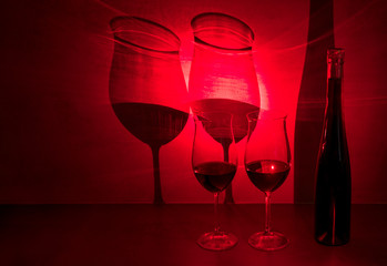 Glasses of red wine (Beaujolais nouveau) cast shadow on gray background with red light