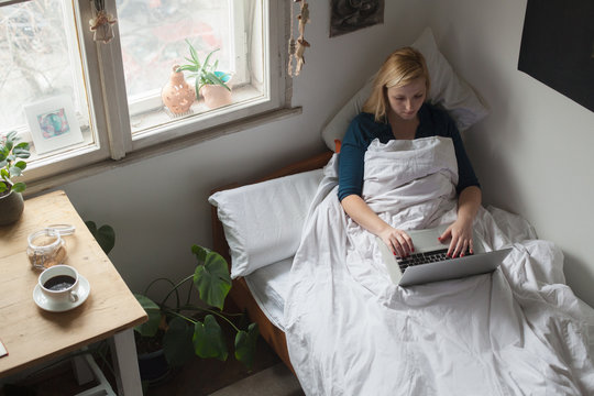 Woman is working on a laptop in her bed