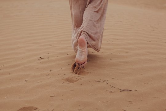 Barefoot unrecognizable woman going away in desert