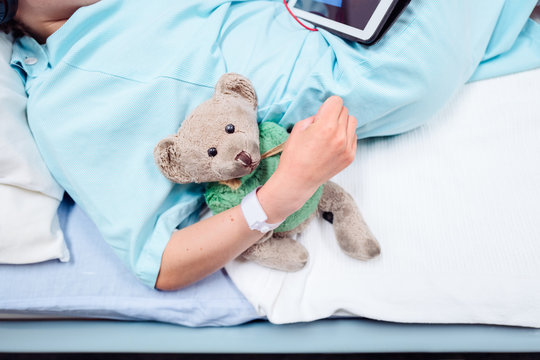 Teddy Bear In The Arm Of A Child In A Hospital Bed