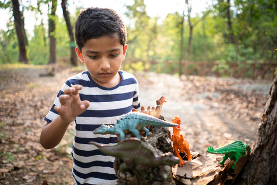 Young boy playing with toy dinosaurs in the forest