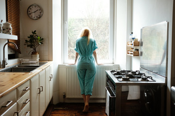 woman wearing a blue jumpsuit looking through the window at the kitchen