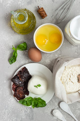 Ingredients for making cake - flour, eggs, milk or buttermilk, olive oil, salt, mozzarella, basil, dried tomatoes. Food background. Copy space.