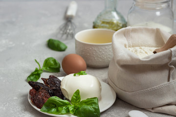 Ingredients for making cake - flour, eggs, milk or buttermilk, olive oil, salt, mozzarella, basil, dried tomatoes. Food background. Copy space.