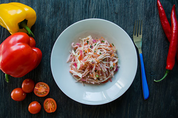 Salad of white cabbage, carrots and bell peppers. Decorated with greens and vegetables. Vegetarian dish. Proper nutrition. Dark wooden background.