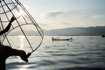 Fisherman balancing with fishing net on boat.