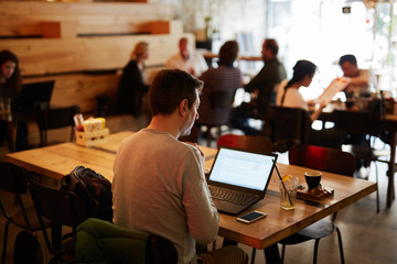 Young businessman working with computer and phone in a cafeteria