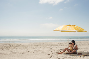 Young mom on beach with baby boy under lemon beach umbrella