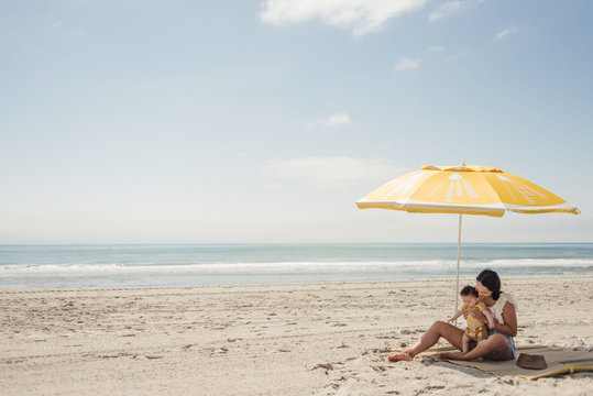 Young mom on beach with baby boy under lemon beach umbrella