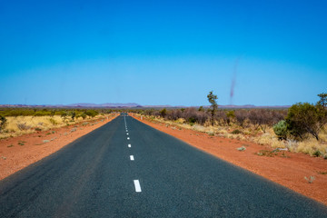 Dust storms besides dark road leading through red sanded Australian landscape towards Karijini National Park