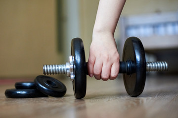 Obraz na płótnie Canvas The hand of the girl takes a dumbbell from the floor at home, home sports, healthy lifestyle