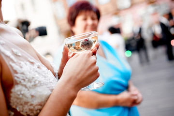 female hands holding a glass of champagne with a frozen berry outside