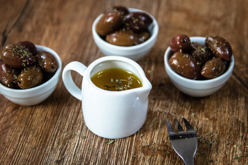 Greek Kalamata black red olives in a small white bowls with spices and small bowl with olive oil on wooden table