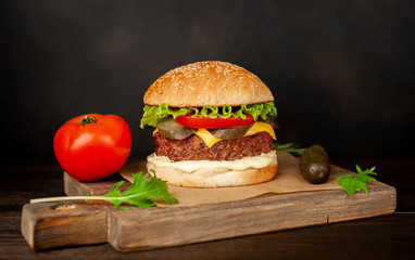 Homemade hamburger with lettuce, tomato, cheese and cucumber on a cutting board