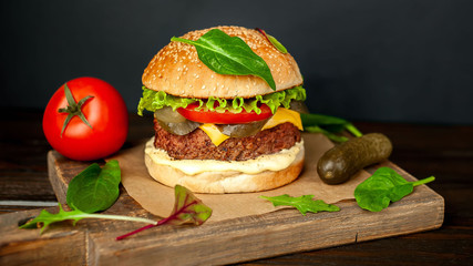 Homemade hamburger with lettuce, tomato, cheese and cucumber on a cutting board