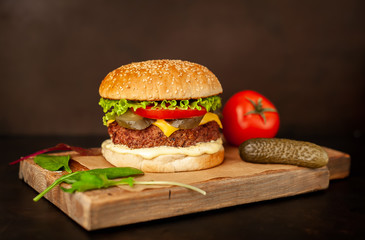 Homemade hamburger with lettuce, tomato, cheese and cucumber on a cutting board