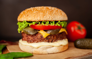 Homemade hamburger with lettuce, tomato, cheese and cucumber on a cutting board
