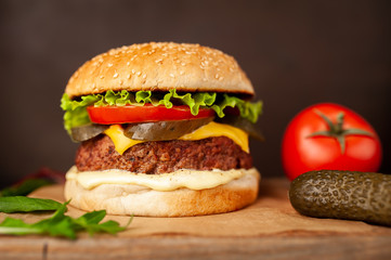 Homemade hamburger with lettuce, tomato, cheese and cucumber on a cutting board