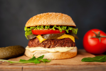 Homemade hamburger with lettuce, tomato, cheese and cucumber on a cutting board