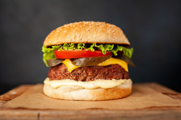 Homemade hamburger with lettuce, tomato, cheese and cucumber on a cutting board