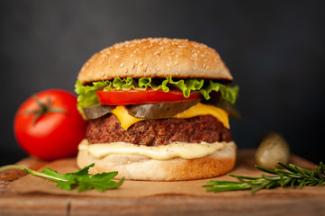 Homemade hamburger with lettuce, tomato, cheese and cucumber on a cutting board