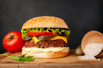 Homemade hamburger with lettuce, tomato, cheese and cucumber on a cutting board