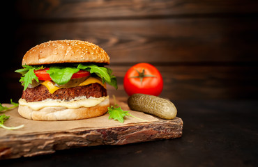 Homemade hamburger with lettuce, tomato, cheese and cucumber on a cutting board