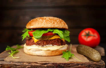 Homemade hamburger with lettuce, tomato, cheese and cucumber on a cutting board