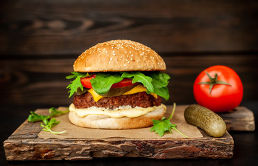 Homemade hamburger with lettuce, tomato, cheese and cucumber on a cutting board