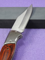 A folding pocket knife with wooden handle propped up on a whetstone. Textured lilac background.