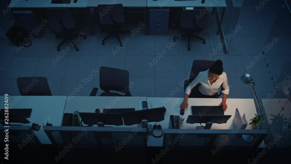 Poster alone working late at night in the office: businesswoman using desktop computer, analyzing, using do