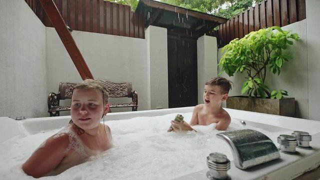 Two young children playing in a spa bath in rain