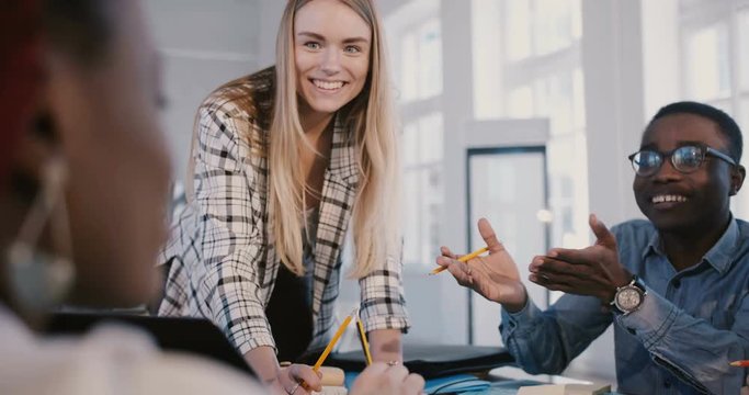 Panning shot of young confident smiling businesswoman leading creative multiethnic team working on brainstorming session