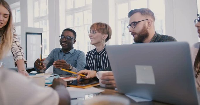 Successful young CEO businesswoman listening to male office worker speaking at creative multiethnic office team meeting.