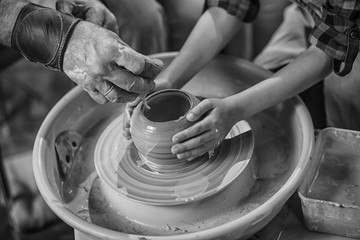 A close-up of the hand of a male potter who teaches his pupil, a child of the art of making a pot or a vase of clay. People working on potters.