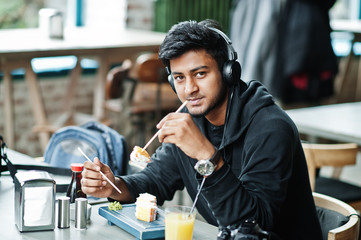 Casual and stylish young asian man with earphones at cafe eating sushi.