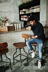 Casual and stylish young asian man with earphones at cafe on bar drinking juice from glass.
