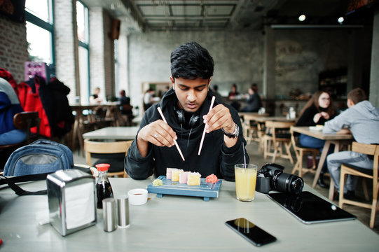 Casual and stylish young asian man with earphones at cafe eating sushi.
