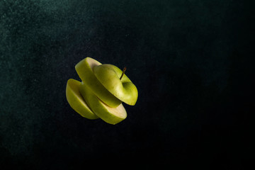 green apple cut into several slices on a dark gradient background.