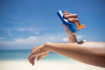 Woman applying sunscreen on her hands from a bottle on the beach with the sea in the background....